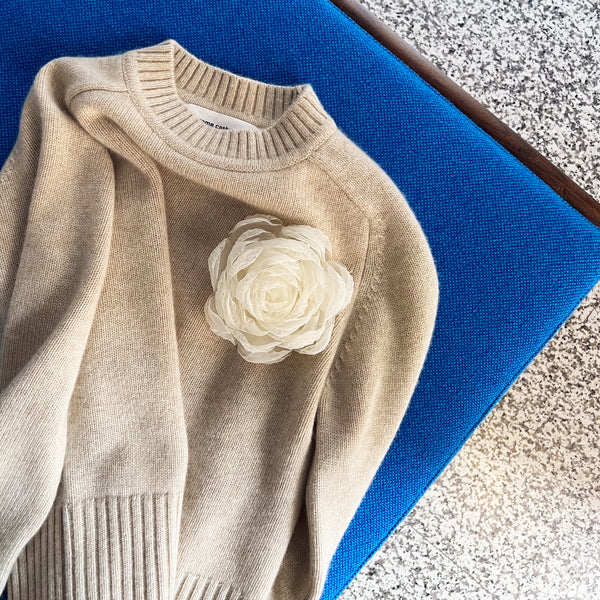 Extreme Cashmere beige sweater with tulle rose brooch laying on a blue daybed 